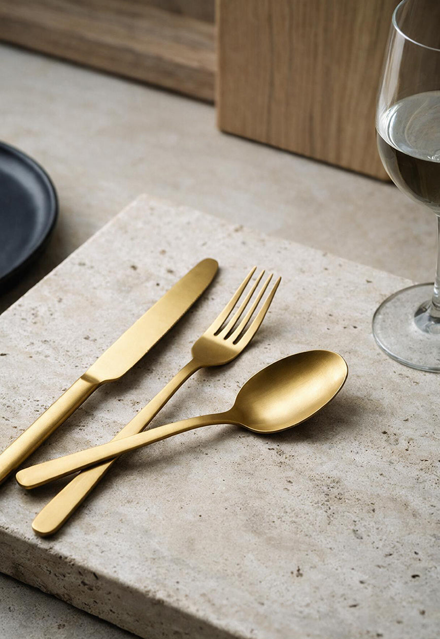 Brushed gold table knife, fork and spoon arranged on a travertine stone slab