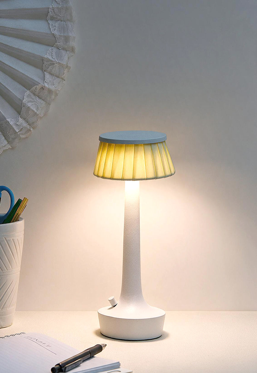 Cordless LED table lamp with a pleated shade lit on a desk beside a notebook