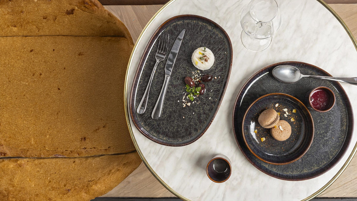Dark stoneware plates with plated fine dining dishes on a marble table